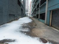 the view up an empty alley in a city with snow on the ground and buildings in the distance