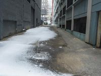 the view up an empty alley in a city with snow on the ground and buildings in the distance