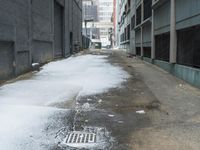 the view up an empty alley in a city with snow on the ground and buildings in the distance