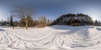 a snow covered road in a field with lots of trees and buildings on the other side