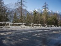 snow covers the top of a fence along a snow covered road in the middle of mountains