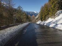 snow covers the top of a fence along a snow covered road in the middle of mountains