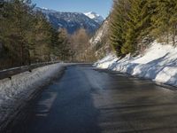 snow covers the top of a fence along a snow covered road in the middle of mountains