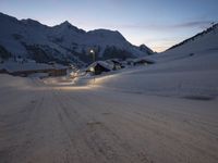 a snow covered road running up the side of a mountain range at dusk with mountains in the background