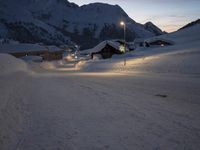 a snow covered road running up the side of a mountain range at dusk with mountains in the background