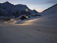 a snow covered road running up the side of a mountain range at dusk with mountains in the background