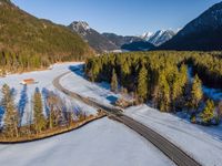 a lone road runs through the snow and trees in front of mountains and valleys,