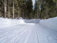 the road is covered by snow with tracks of skis on it and trees to the side