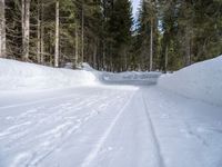 the road is covered by snow with tracks of skis on it and trees to the side