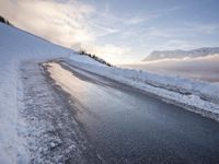 snow covered road beside large mountain in distance and sky in the background with clouds overhead