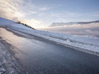 snow covered road beside large mountain in distance and sky in the background with clouds overhead