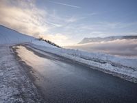 snow covered road beside large mountain in distance and sky in the background with clouds overhead