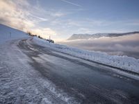 snow covered road beside large mountain in distance and sky in the background with clouds overhead