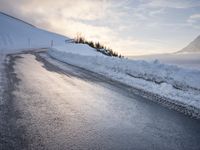 snow covered road beside large mountain in distance and sky in the background with clouds overhead