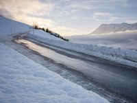 snow covered road beside large mountain in distance and sky in the background with clouds overhead