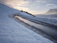 snow covered road beside large mountain in distance and sky in the background with clouds overhead