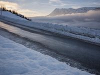 snow covered road beside large mountain in distance and sky in the background with clouds overhead