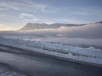 snow covered road beside large mountain in distance and sky in the background with clouds overhead