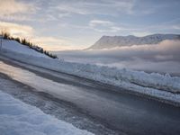 snow covered road beside large mountain in distance and sky in the background with clouds overhead