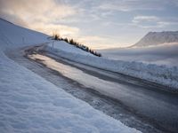 snow covered road beside large mountain in distance and sky in the background with clouds overhead