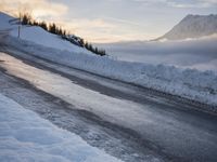 snow covered road beside large mountain in distance and sky in the background with clouds overhead