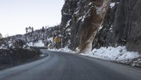 a curve in the road with snow covering it and rocks near by it, on the side of a mountain