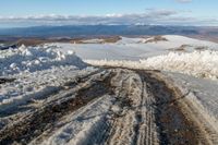 a snowy road surrounded by snow and mountains in the background with clouds in the sky