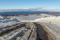 a snowy road surrounded by snow and mountains in the background with clouds in the sky