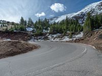 the curved road is near an evergreen mountain side area with rocks and trees in winter