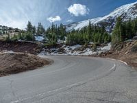 the curved road is near an evergreen mountain side area with rocks and trees in winter