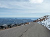 an empty road and a hill overlook the view of mountains and clouds and blue sky