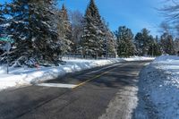 an empty country road in the winter snow with some trees and snow on one side and trees to the other