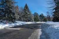 an empty country road in the winter snow with some trees and snow on one side and trees to the other