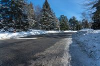 an empty country road in the winter snow with some trees and snow on one side and trees to the other