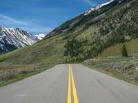 the road is paved with yellow markings and has a snowy mountain range in the background