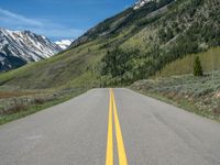 the road is paved with yellow markings and has a snowy mountain range in the background