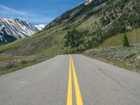 the road is paved with yellow markings and has a snowy mountain range in the background