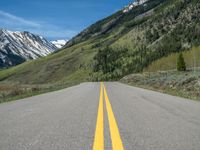 the road is paved with yellow markings and has a snowy mountain range in the background