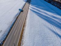 an aerial view of cars travelling in the snow on a road near a forest on a bright sunny day