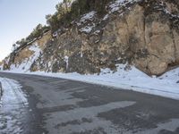 a snow skier is skiing down the snowy road side of the mountain with rocky cliffs