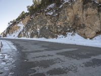 a snow skier is skiing down the snowy road side of the mountain with rocky cliffs