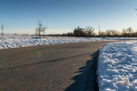 the long road runs along both sides of the snow covered field with no people on it