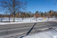 an empty street surrounded by snow and trees on a clear day in winter day with blue sky