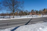 an empty street surrounded by snow and trees on a clear day in winter day with blue sky