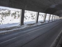 a car is driving through the snow covered roadway near a bridge on a mountain side