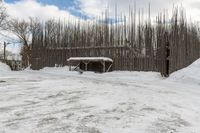 a barn with a roof covered in snow near many trees and small piles of snow