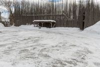 a barn with a roof covered in snow near many trees and small piles of snow