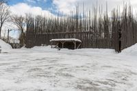 a barn with a roof covered in snow near many trees and small piles of snow