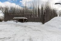 a barn with a roof covered in snow near many trees and small piles of snow