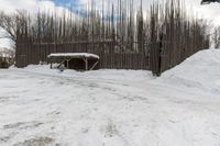 a barn with a roof covered in snow near many trees and small piles of snow